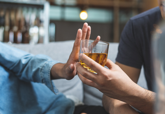 Cropped image of a man handing a cup of alcoholic drink to a teen