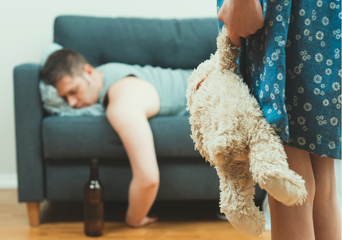 A daughter holding a stuffed toy looking at his intoxicated father lying on the couch