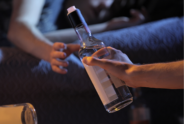 Cropped image of a man giving an alcoholic drink to a teen